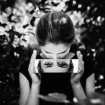 Femme tenant un miroir où se reflète ses yeux, symbolisant le regard des autres et la perception de soi.